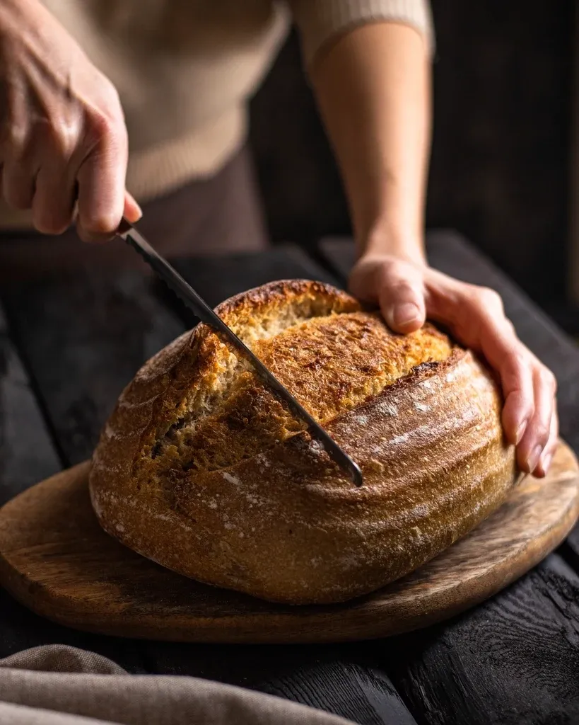 A baker cutting into a fresh sourdough loaf