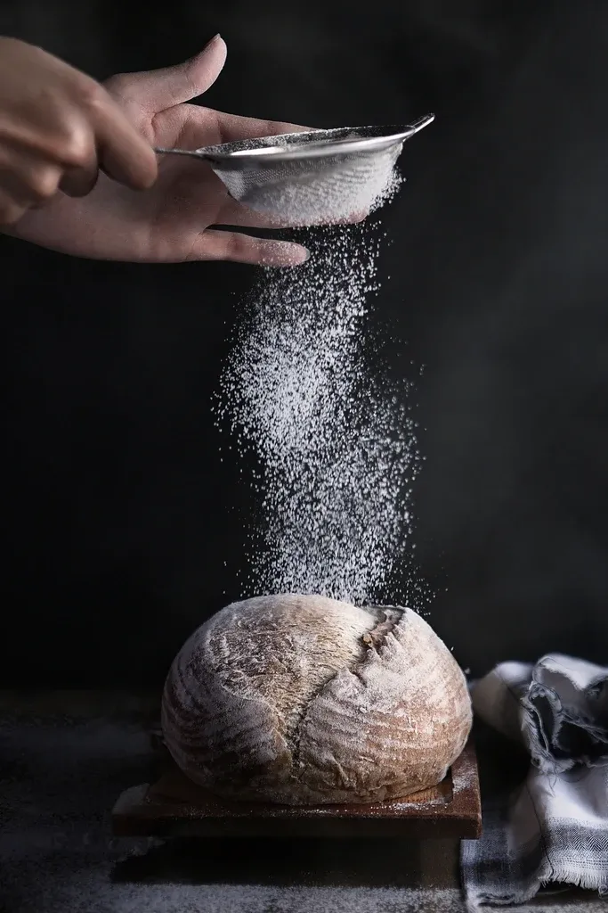 Flour being sifted over a loaf in a dark kitchen